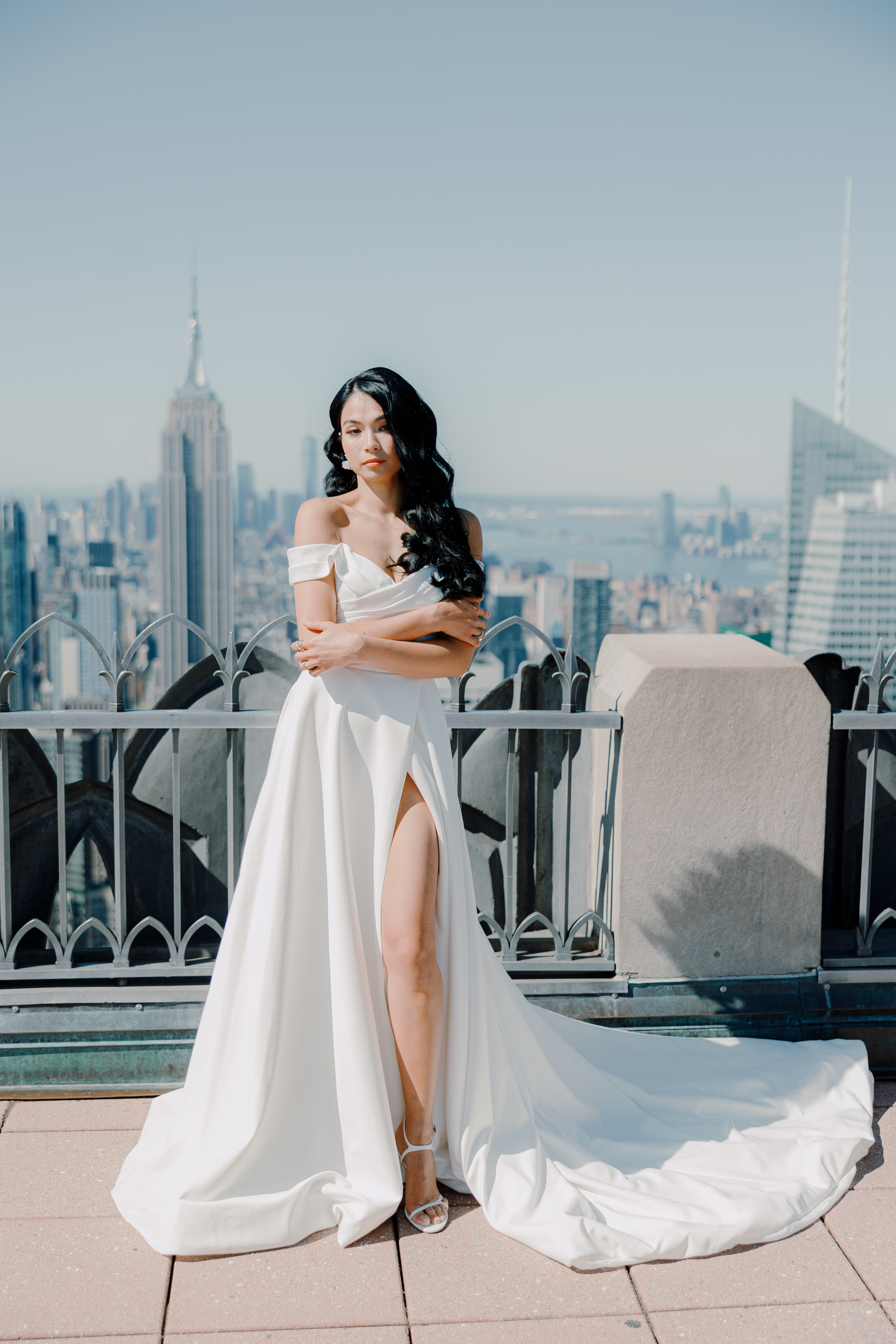 Bride on rooftop; off-shoulder gown, Hollywood waves; natural glam with city skyline.
