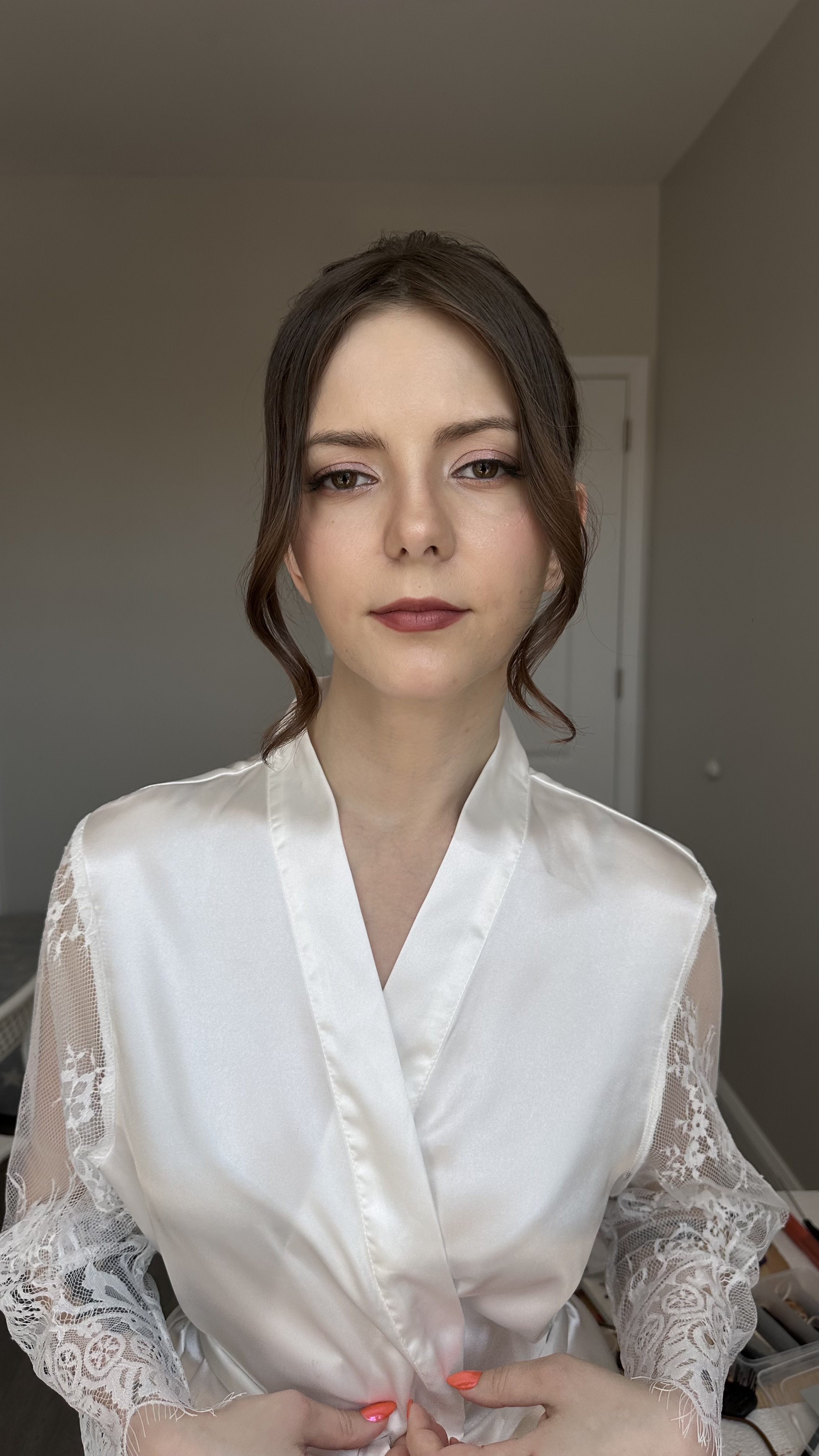 Bride in a white satin robe with lace sleeves, romantic makeup.