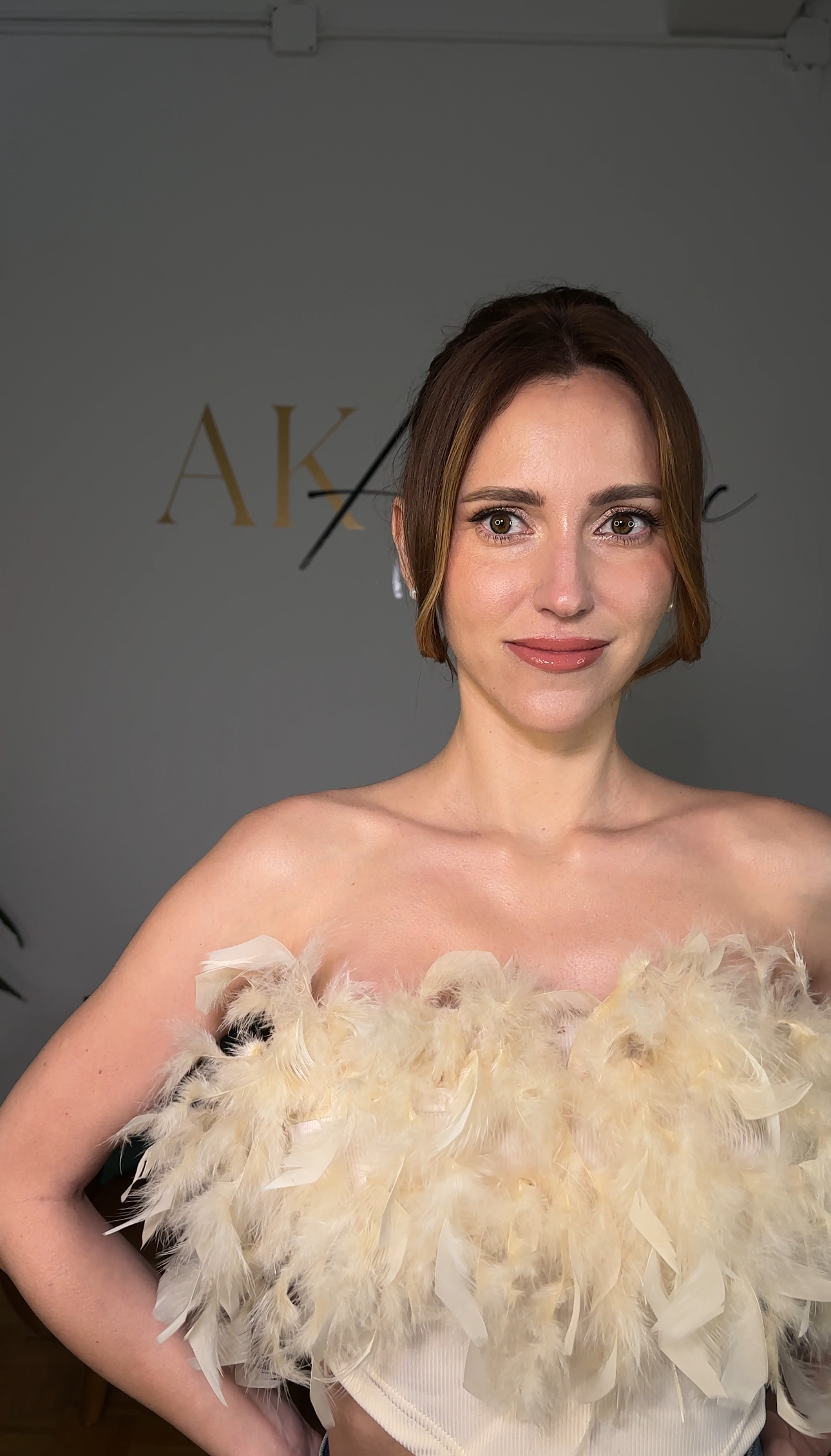 Half-turn portrait; soft nude makeup, updo, feathered beige top.