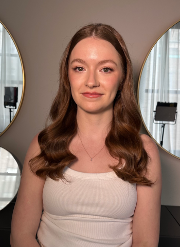 Woman with soft waves and natural makeup in a white top; studio mirrors.