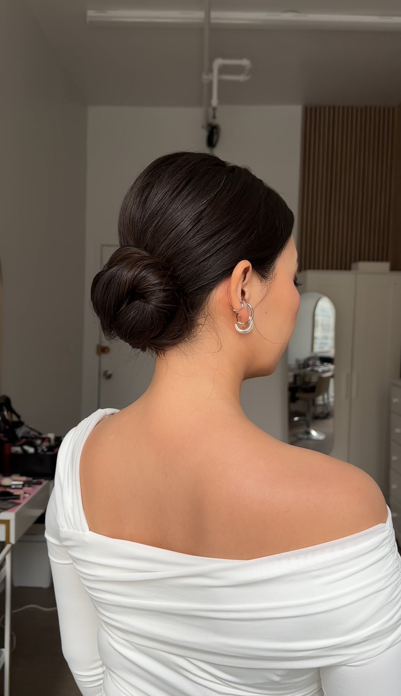 Back view: sleek low bun, bare shoulder, silver hoop earrings.