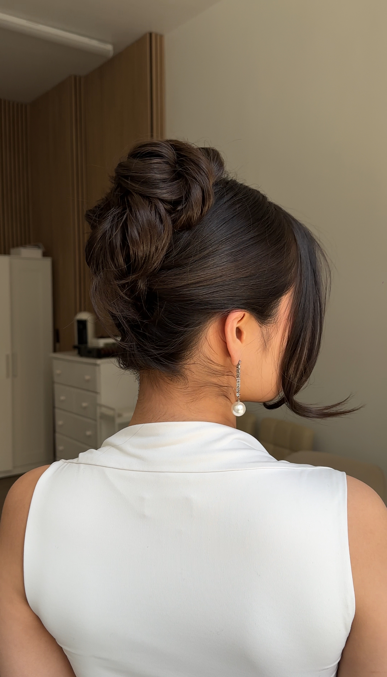 Rear three-quarter view: full textured updo, face-framing strand, pearl earring.